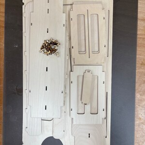 May include: A set of unfinished wooden pieces for building a small wooden box. The pieces are arranged on a dark surface. The pieces are made of light wood and have a smooth finish.