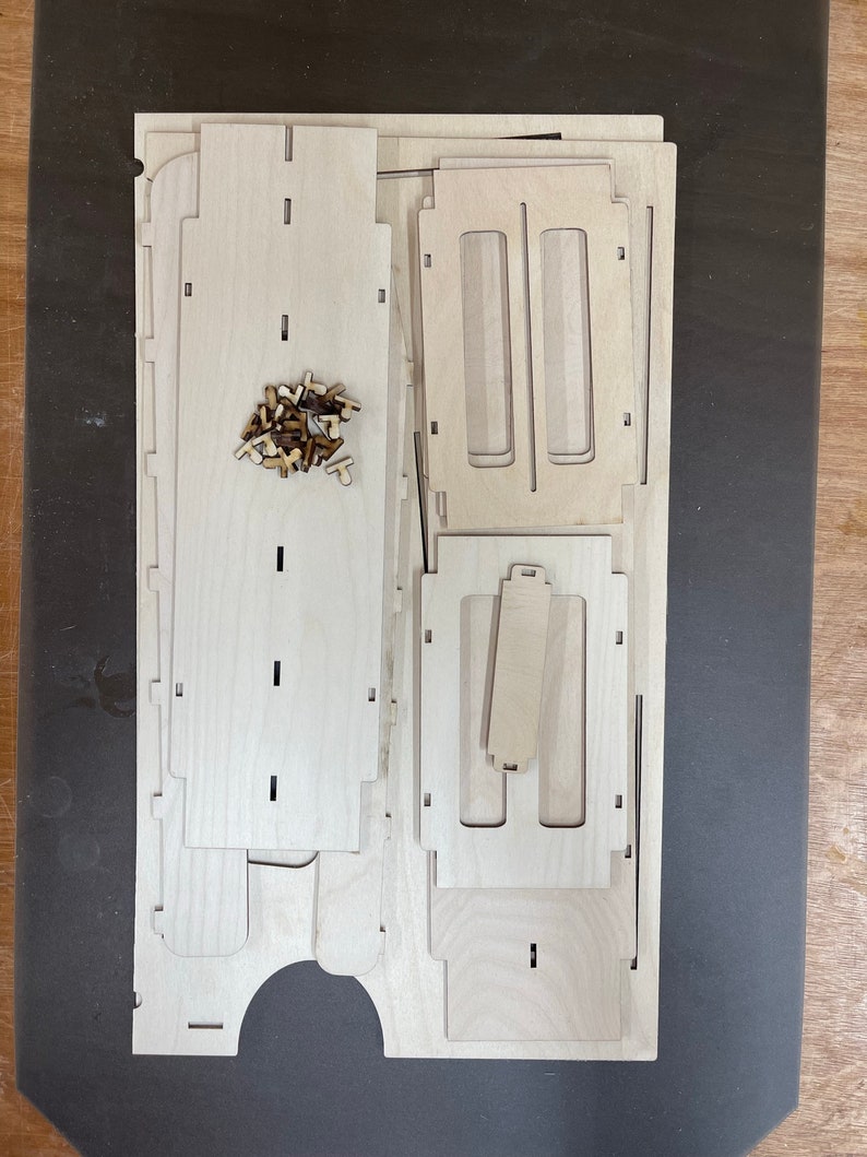 May include: A set of unfinished wooden pieces for building a small wooden box. The pieces are arranged on a dark surface. The pieces are made of light wood and have a smooth finish.