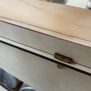 May include: Close-up of a wooden box with a brown latch. The box is made of light wood and has a smooth finish.