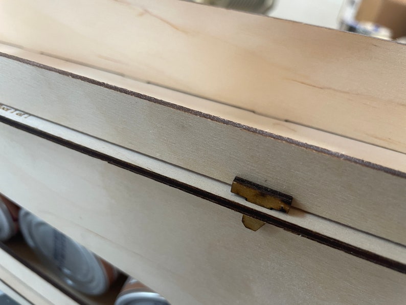 May include: Close-up of a wooden box with a brown latch. The box is made of light wood and has a smooth finish.