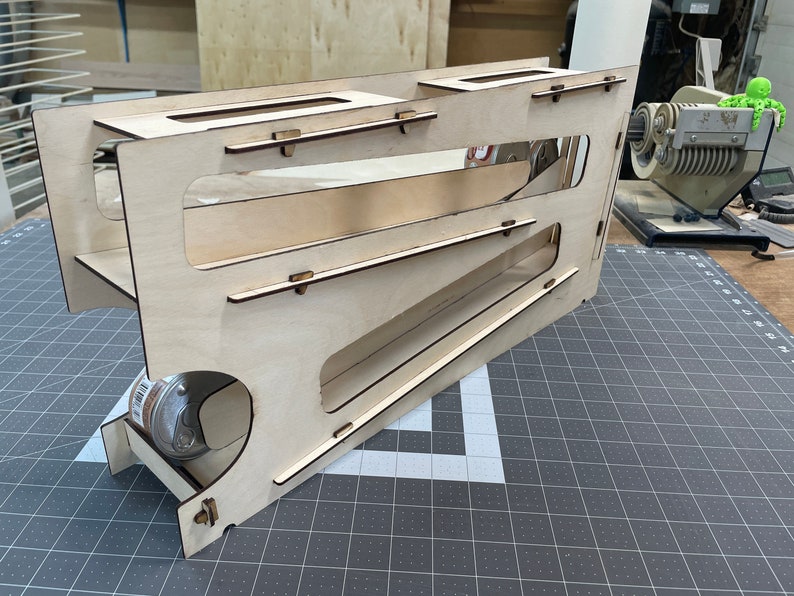 May include: A wooden toy with a ramp and a small wheel at the bottom. The toy is made of light brown wood and has a natural finish.