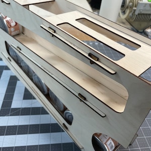 May include: A wooden storage organizer with multiple shelves for holding cans. The organizer is made of light wood and has a natural finish. The shelves are designed to hold cans of various sizes.