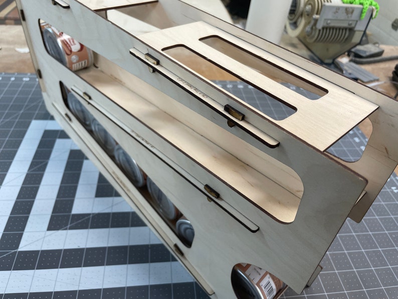 May include: A wooden storage organizer with multiple shelves for holding cans. The organizer is made of light wood and has a natural finish. The shelves are designed to hold cans of various sizes.