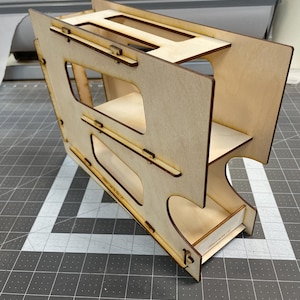 May include: A wooden organizer with three shelves, each with a cutout for holding items. The organizer is made of light brown wood and has a natural finish.