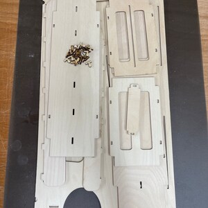 May include: A set of unfinished wooden pieces for building a small wooden box. The pieces are arranged on a dark surface. The pieces are made of light wood and have a smooth finish.