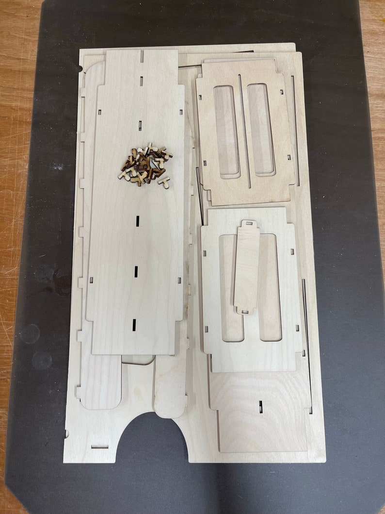 May include: A set of unfinished wooden pieces for building a small wooden box. The pieces are arranged on a dark surface. The pieces are made of light wood and have a smooth finish.