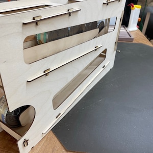 May include: A wooden can dispenser with multiple shelves for storing and dispensing cans. The dispenser is made of light wood and has a natural finish. The dispenser is empty and ready to be filled with cans.