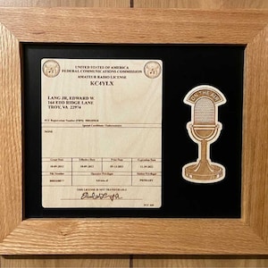 May include: A framed amateur radio license with the call sign KC4YLX, issued to Edward W. Lang Jr. The license is dated 10-09-2012 and expires 11-29-2022. The license is framed with a black mat and a wooden frame. A sticker with the text "ON THE AIR" and a microphone graphic is on the right side of the frame.