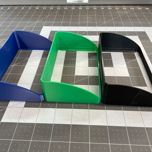 May include: Three 3D printed plastic trays, one blue, one green, and one black. The trays are stacked on top of each other.