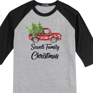 May include: A gray raglan baseball shirt with black sleeves. The front features a red truck carrying a Christmas tree, with the text "Sewell Family Christmas" in black script.