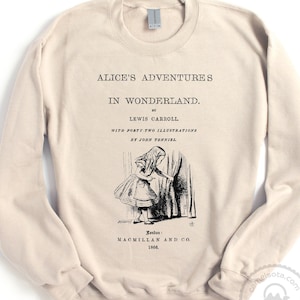 May include: A beige sweatshirt with a black print of the cover of the book "Alice's Adventures in Wonderland" by Lewis Carroll. The print includes an illustration of Alice looking through a door.