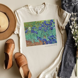 May include: A white t-shirt with a print of Vincent van Gogh's "Irises" painting. The painting features a field of blue irises with green leaves and a white background. The text "Irises, 1889, Oil on canvas by Vincent van Gogh" is printed below the painting.