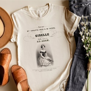 May include: A beige t-shirt with a vintage print of a ballerina. The print features the text "Danse par Mlle. Carlotta Grisi & M. Petipa. (1841) Giselle. Ballet. Compose par AD. ADAM."