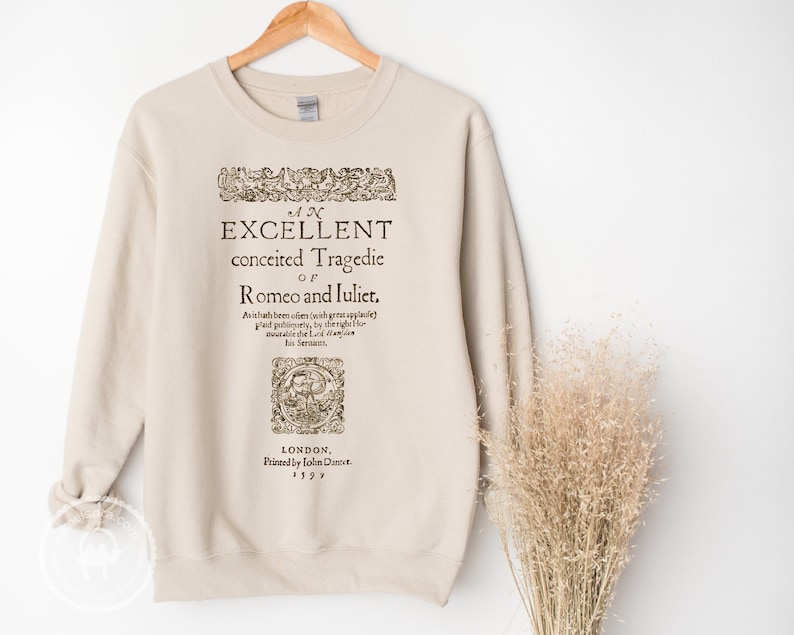 May include: A beige sweatshirt with a vintage-style print of the title page of "Romeo and Juliet" by William Shakespeare. The text reads "An Excellent Conceited Tragedie of Romeo and Juliet" and includes the publication date of 1597.