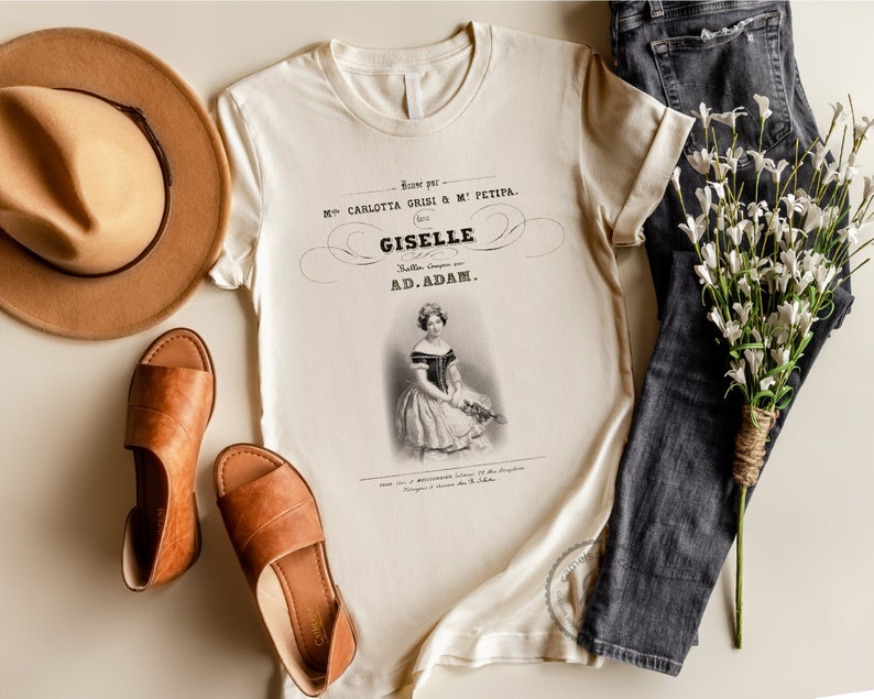 May include: A beige t-shirt with a vintage print of a ballerina. The print features the text "Danse par Mlle. Carlotta Grisi & M. Petipa. (1841) Giselle. Ballet. Compose par AD. ADAM."