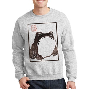 May include: A gray sweatshirt with a black and white illustration of a frog in a square frame. The illustration has a red stamp with Japanese characters in the upper right corner.
