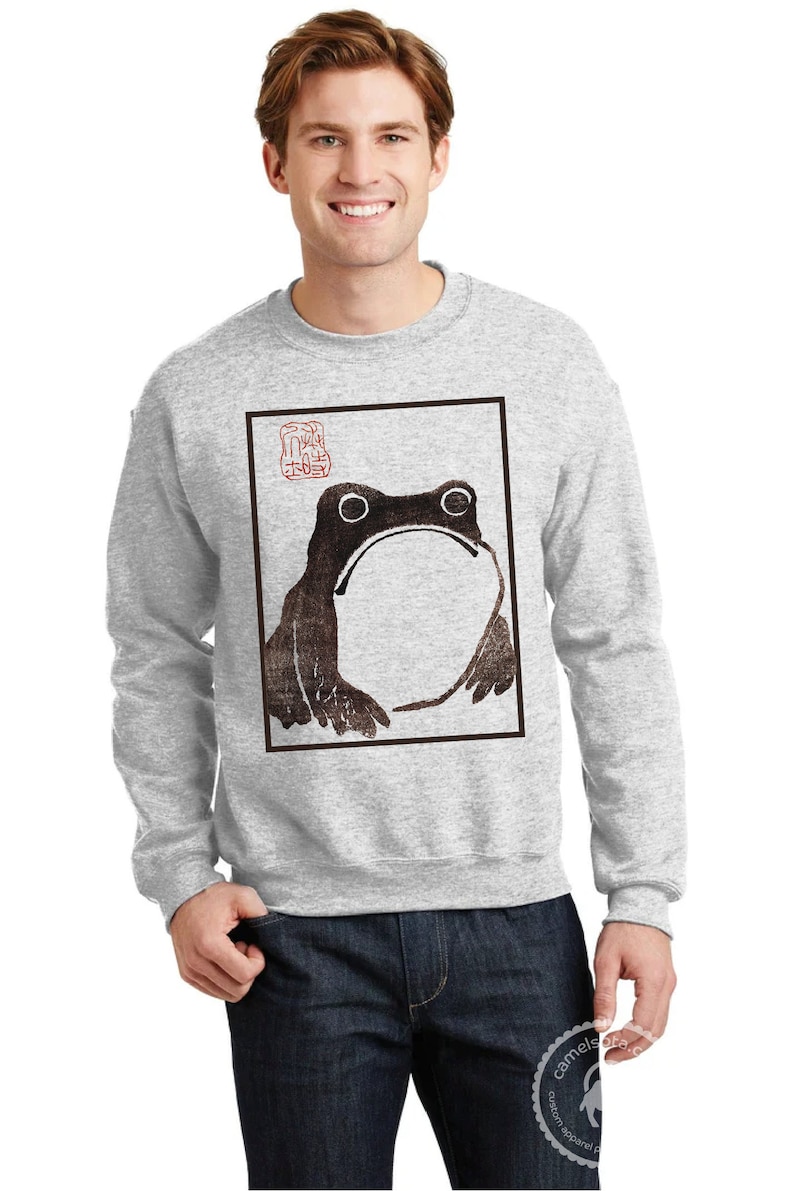 May include: A gray sweatshirt with a black and white illustration of a frog in a square frame. The illustration has a red stamp with Japanese characters in the upper right corner.