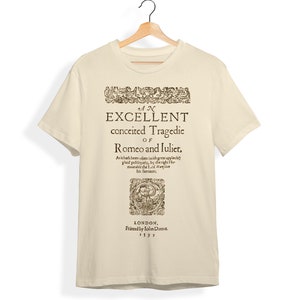 May include: A beige t-shirt with a vintage-style print of the title page of "An Excellent Conceited Tragedie of Romeo and Juliet." The text is in black and the print includes a decorative border and a small illustration. The text reads: "As ithath been often (with great applause) plaid publiquely, by the right Honourable the Lo: Hanjden his Sernants. LONDON, Printed by Lolin Dantet. 1597."