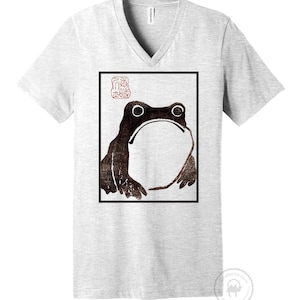 May include: A gray V-neck t-shirt with a black and white image of a frog in a square frame. The image is a Japanese woodblock print with a red seal in the upper left corner.
