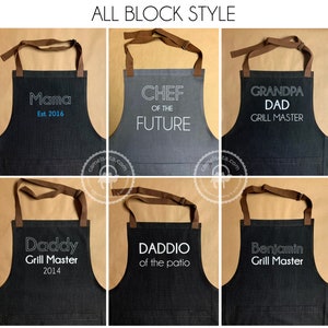 K&ouml;nnte beinhalten: Sechs verschiedene Sch&uuml;rzen mit unterschiedlichen Texten. Die Sch&uuml;rzen sind schwarz und grau mit braunen Tr&auml;gern. Der Text auf den Sch&uuml;rzen lautet "Mama Est. 2016", "Chef of the Future", "Grandpa Dad Grill Master", "Daddy Grill Master 2014", "Daddio of the Patio" und "Benjamin Grill Master".