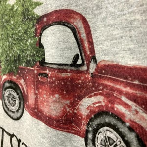 May include: A red vintage truck carrying a green Christmas tree, with a snowy effect, printed on a gray background. The truck has black tires and silver rims. The image has the text "Christmas" in a cursive font.