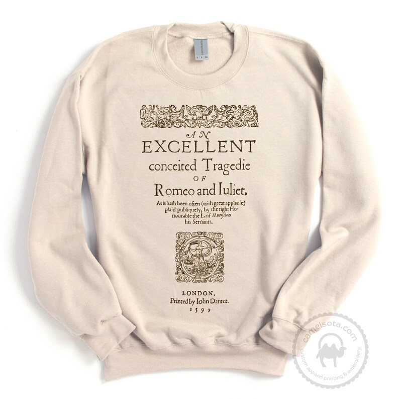 May include: A beige sweatshirt with a vintage-style print of the title page of "Romeo and Juliet" by William Shakespeare. The text reads "An Excellent Conceited Tragedie of Romeo and Juliet." The print also includes the date "1599" and the name of the printer, "John Danter."