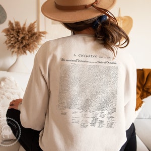 May include: A beige sweatshirt with the text "In Congress, July 4, 1776" and the full text of the Declaration of Independence printed on the back.
