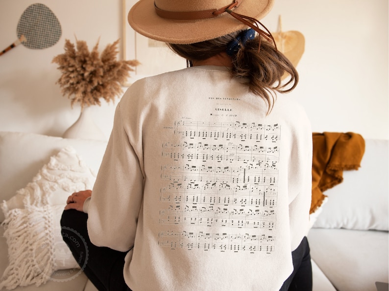 May include: A beige sweatshirt with a vintage sheet music design printed on the back. The music is for a song called "Gavotte" and includes the text "Pour mes petites" at the top.