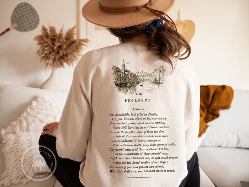 May include: A beige sweatshirt with a vintage illustration of a city scene and text that reads "The Prologue, Chorus. Two households, both alike in dignity, (In fair Verona, where we lay our scene,) From ancient grudge break to new mutiny, Where civil blood makes civil hands unclean. From forth the fatal loins of these two foes A pair of star-cross'd lovers take their life; Whose misadventured piteous overthrows Doth, with their death, bury their parents' strife. The fearful passage of their death-mark'd love, And the continuance of their parents' rage, Which, but their children's end, nought could remove, Is now the two hours' traffic of our stage; The which if you with patient ears attend, What here shall miss, our toil shall strive to mend."