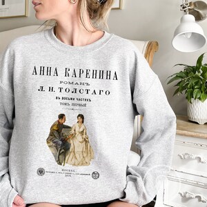 May include: Gray sweatshirt with a vintage book cover design featuring a black and white illustration of a couple. The text on the cover reads "Anna Karenina, Roman L.N. Tolstoy, in eight parts, volume one".