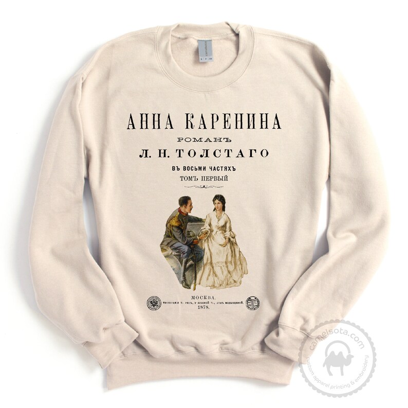 May include: A beige sweatshirt with a vintage-style print of the book cover for "Anna Karenina" by Leo Tolstoy. The cover features an illustration of two people in 19th-century clothing.