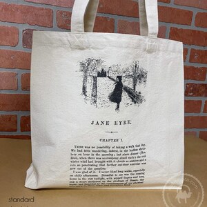May include: A white canvas tote bag with black handles. The bag features a black and white illustration of a woman walking down a path, with trees on either side. The text "JANE EYRE" and "CHAPTER I." is printed on the bag.