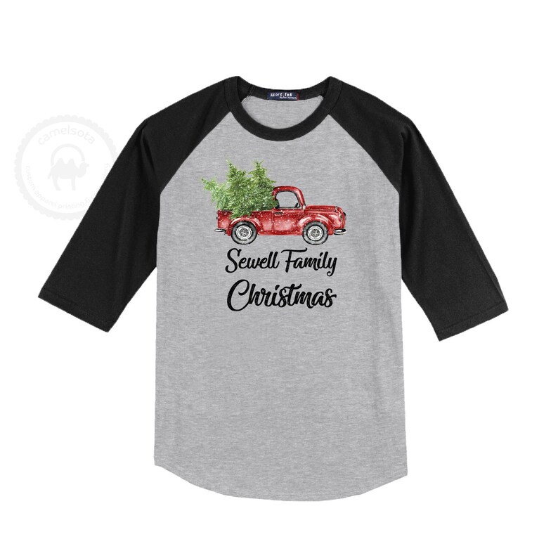 May include: A gray raglan baseball shirt with black sleeves. The front features a red truck carrying a Christmas tree, with the text "Sewell Family Christmas" in black script.