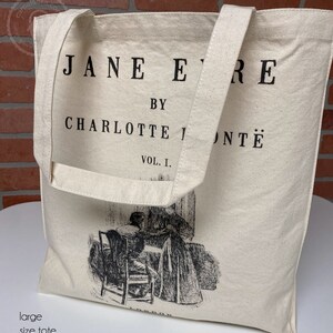 May include: A white canvas tote bag with black handles and the text "JANE EYRE BY CHARLOTTE BRONT&Euml; VOL. I." printed on the front. The bag features a black and white illustration of two women sitting at a table.