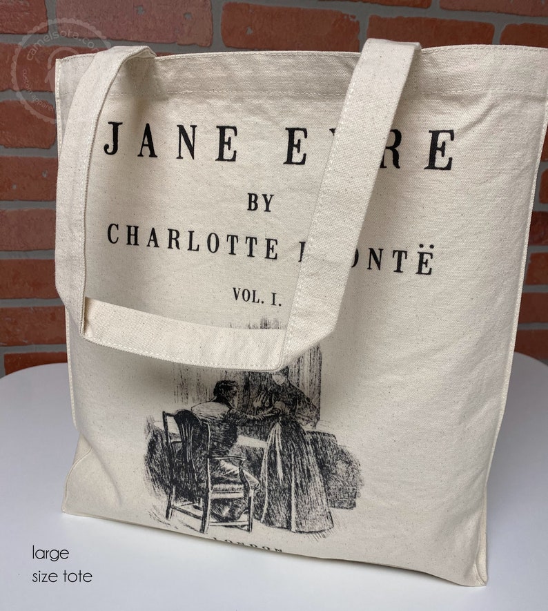 May include: A white canvas tote bag with black handles and the text "JANE EYRE BY CHARLOTTE BRONT&Euml; VOL. I." printed on the front. The bag features a black and white illustration of two women sitting at a table.