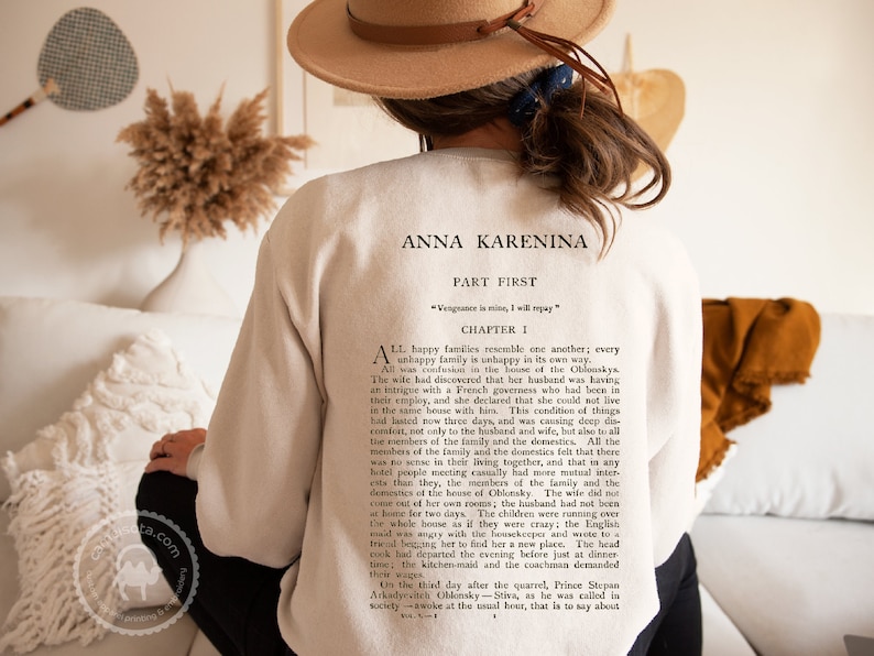 May include: A white sweatshirt with a black print of a book page featuring the title "Anna Karenina" and the first chapter of the novel. The text reads "All happy families resemble one another; every unhappy family is unhappy in its own way."