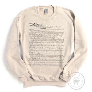 May include: A beige sweatshirt with the full text of the US Constitution printed on the front. The text includes the phrase "We the People".