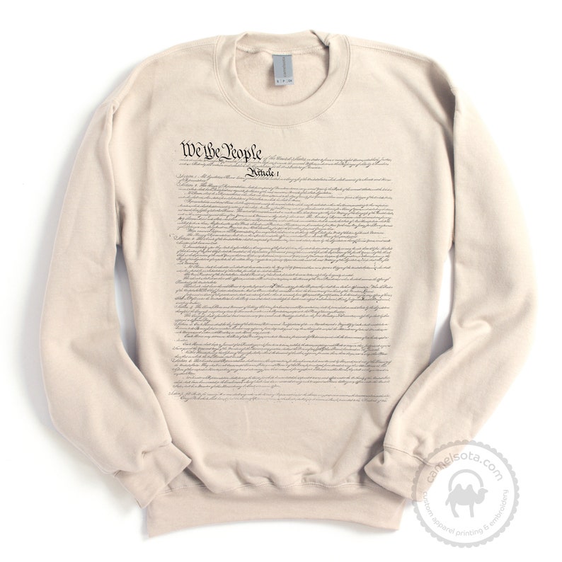 May include: A beige sweatshirt with the full text of the US Constitution printed on the front. The text includes the phrase "We the People".
