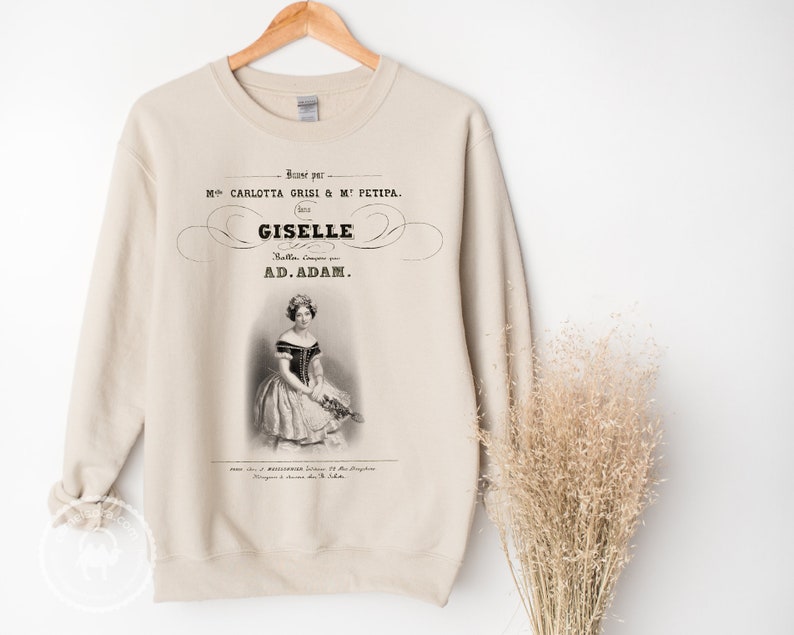 May include: A beige sweatshirt with a vintage-style print of a ballerina in a white dress. The print includes the text "Giselle" and "Ad. Adam."