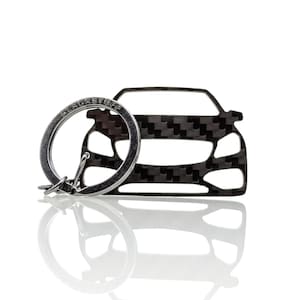 May include: A silver car key chain with a black carbon fiber design. The keychain features a ring with the word "BLACKSTUFF" engraved on it.