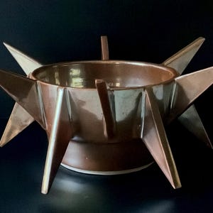 Peut inclure: Un bol en céramique marron doté d'une base circulaire et d'une série de pointes triangulaires acérées en forme d'étoile s'étendant vers l'extérieur depuis le bord. Le bol présente une finition lisse et brillante d'une couleur marron uniforme.