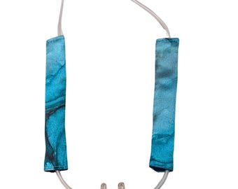 May include: A clear plastic nasal cannula with two prongs, connected to a clear plastic tube with blue and white patterned fabric covers on each end.