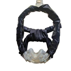 May include: A CPAP mask featuring a clear plastic nasal cushion and black fabric headgear. The headgear is made of a soft, flexible material designed for comfort. The mask includes a clear plastic connector.