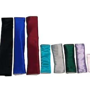 Puede incluir: Surtido de diez cojines rectangulares cubiertos de tela en varios colores, incluyendo negro, azul, rojo, turquesa, gris, verde, morado y rosa.