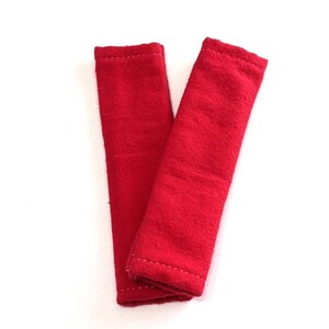 May include: Two red fabric strips with white stitching. The strips are folded in half and are about 10 inches long.