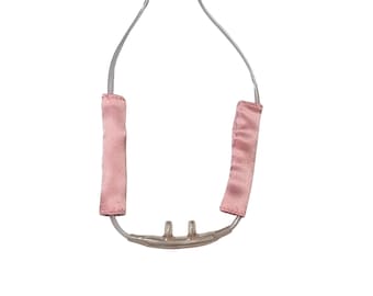 May include: A clear plastic nasal cannula with two prongs and a pink fabric strap. The strap is attached to the cannula with a clear plastic tube.