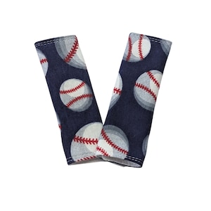 May include: A pair of blue fabric seatbelt covers with a white and red baseball pattern.