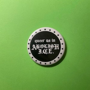May include: A round white button with a black center and the text "queer as in ABOLISH I.C.E." in a gothic font. The button is surrounded by a ring of small black stars. The background is a solid green color.