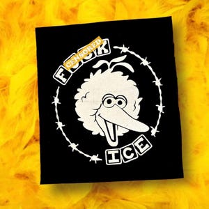 May include: Black square patch featuring a cartoon character with a long beak, surrounded by a barbed wire circle. The words "FUCK" and "ICE" are visible, with "CENSORED" over the "K". The character is white, with a yellow background.