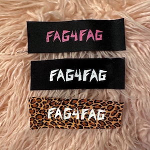 May include: Three rectangular fabric labels with the text "FAG4FAG". The top label is black with pink text, the middle is black with white text, and the bottom is leopard print with white text.